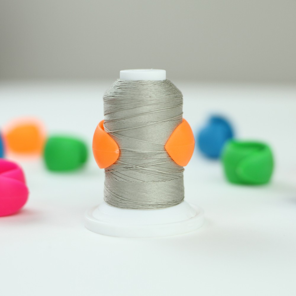 Orange Gypsy Quilter Thread Peel holding a loose thread end against a sewing thread spool