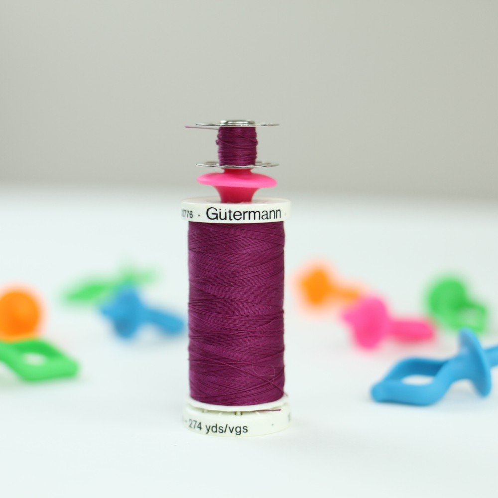 Pink Gypsy Quilter Bobbini holding a wound metal bobbin with its matching thread spool